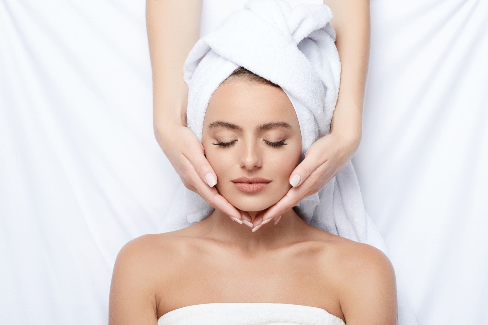 A client having a facial, with the therapist’s hands resting at her temples.